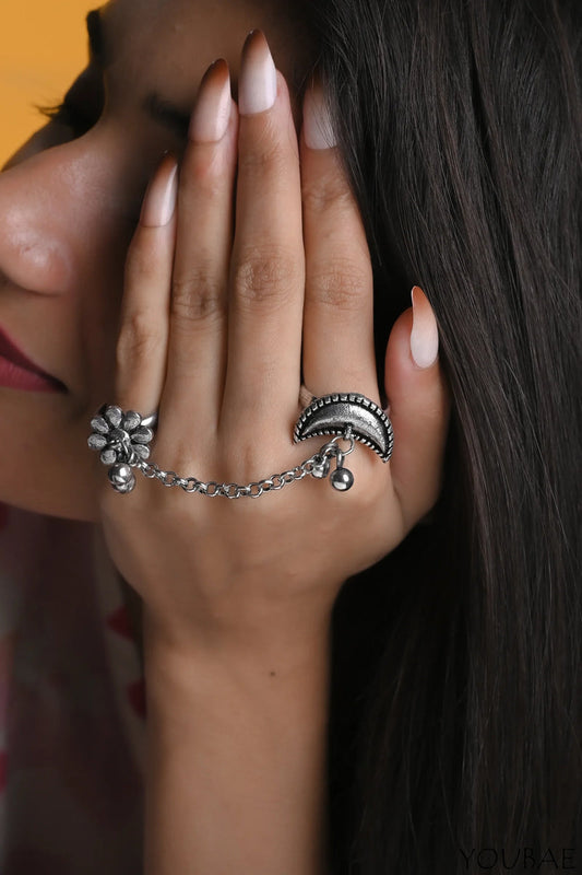 Close-up of a hand wearing a silver ring with floral design and dangling elements.