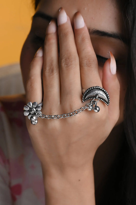 Close-up of a hand wearing a silver ring with floral design and chain, against a blurred background.